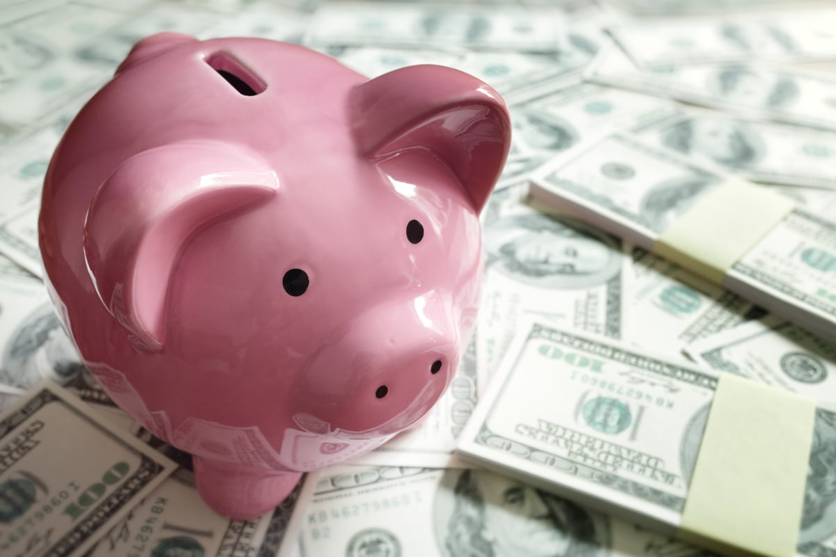 A pink piggy bank on top of a pile of money.
