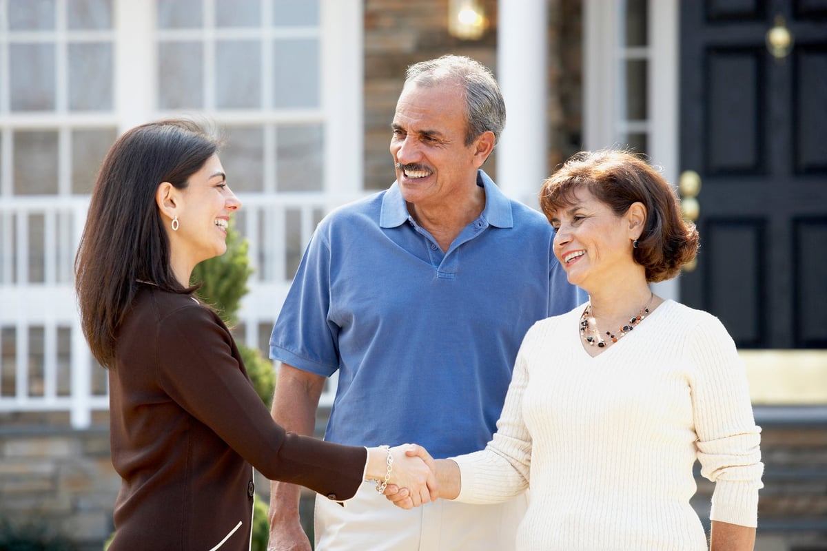 Realtor shaking hands with mature couple outside home.