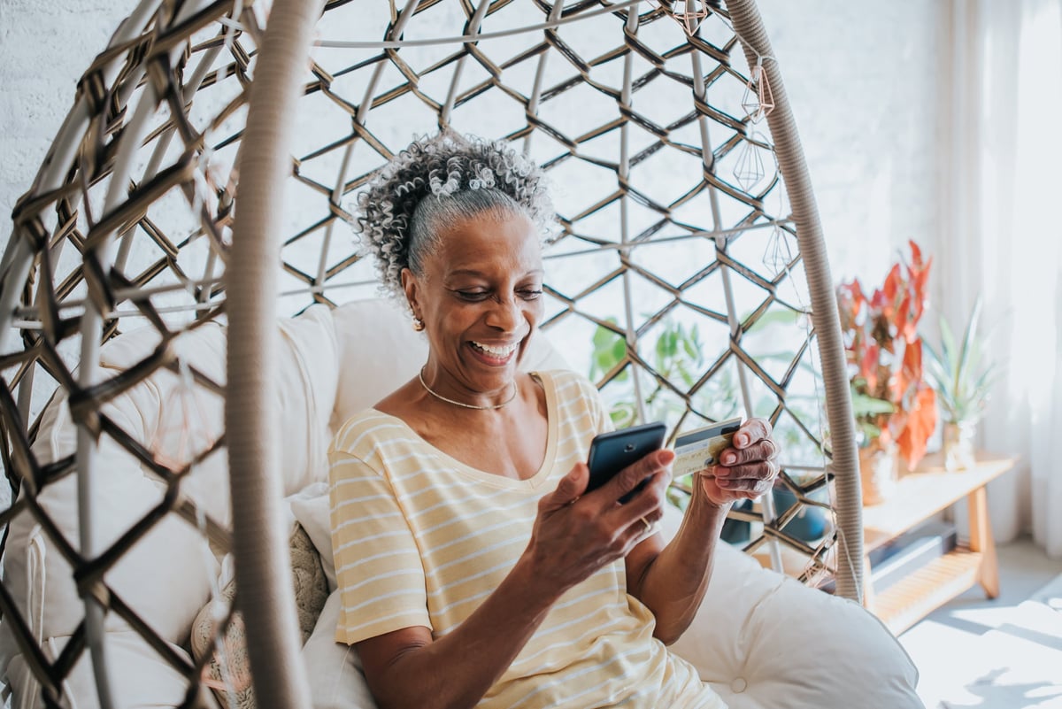 Senior woman holding a credit card and her cell phone smiling.