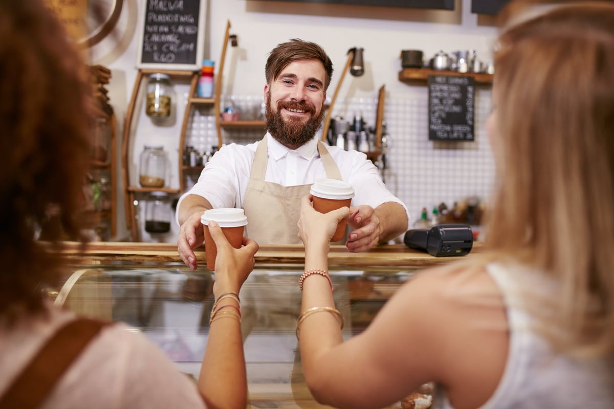 Smiling barista hands coffee to two women