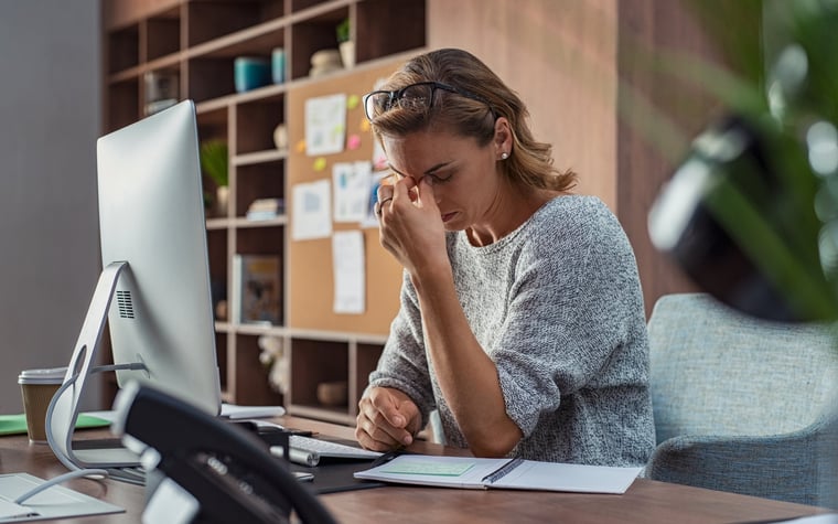 Stressed businesswoman sitting at computer with hand on face.