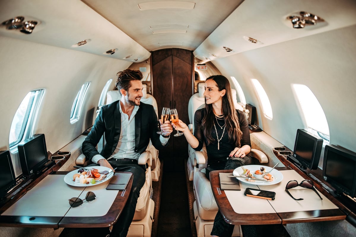 Successful couple making a toast with champagne glasses while having canapes aboard a private airplane