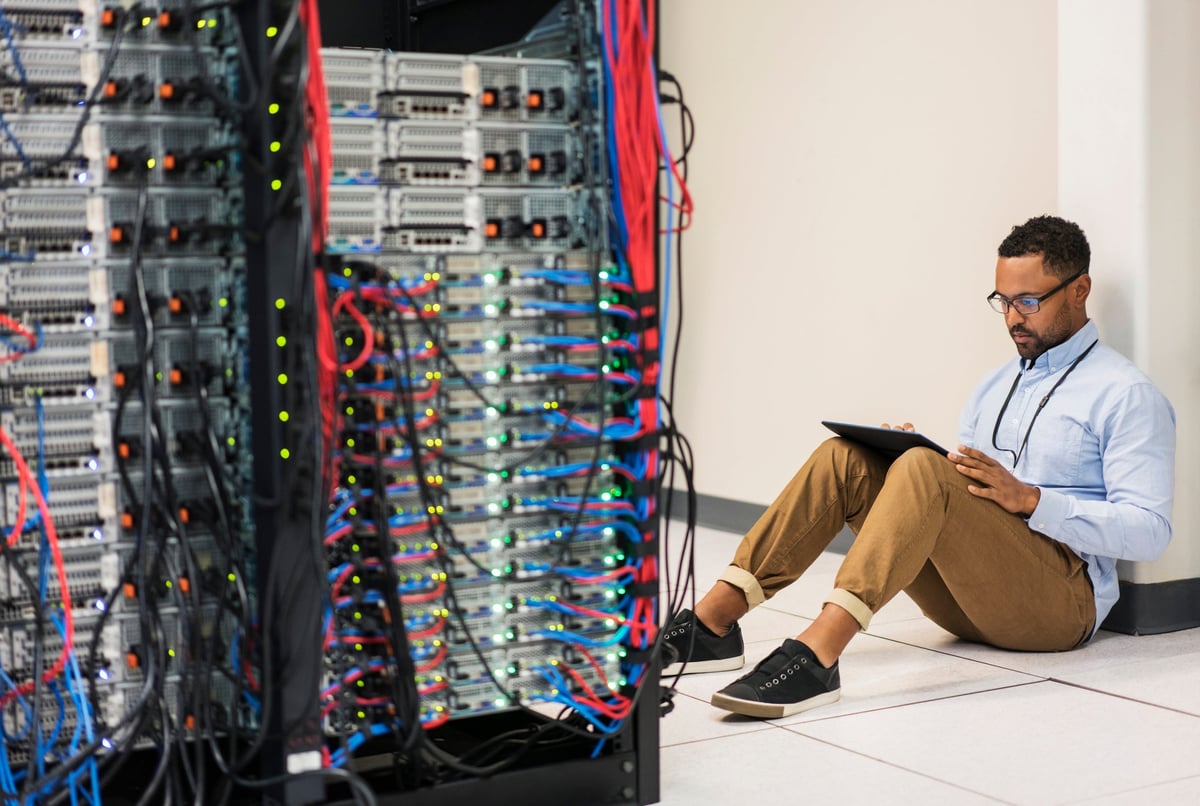 Technician sitting on floor with tablet in a server room.