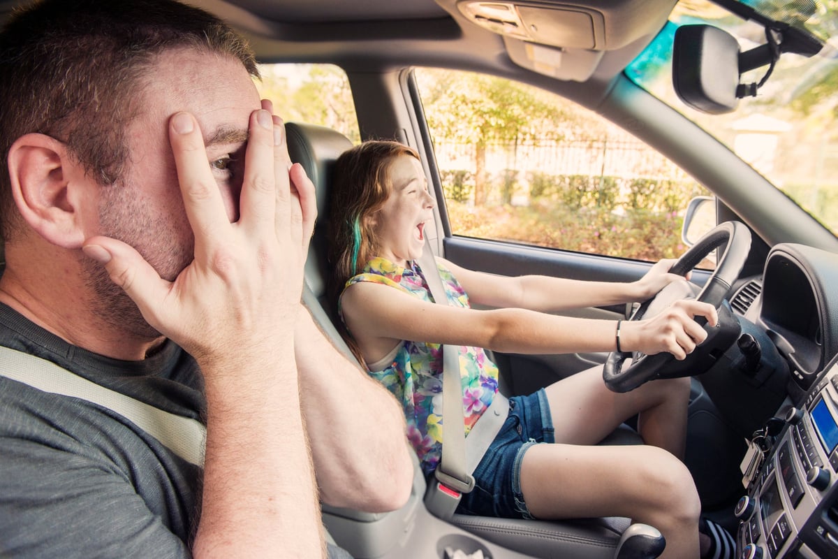 A parent covers his face in fear as his overly excited daughter drives.