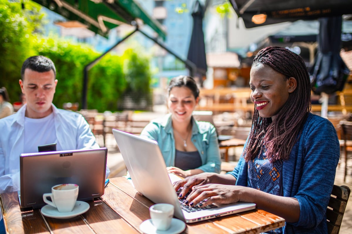 Three adults sitting on a patio utilizing their laptops.