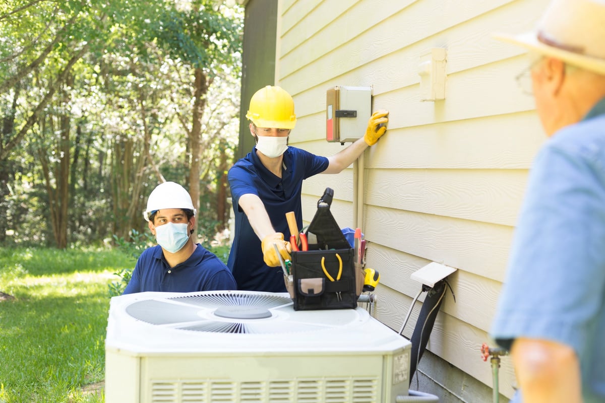 Two air conditioner workers service outside unit.