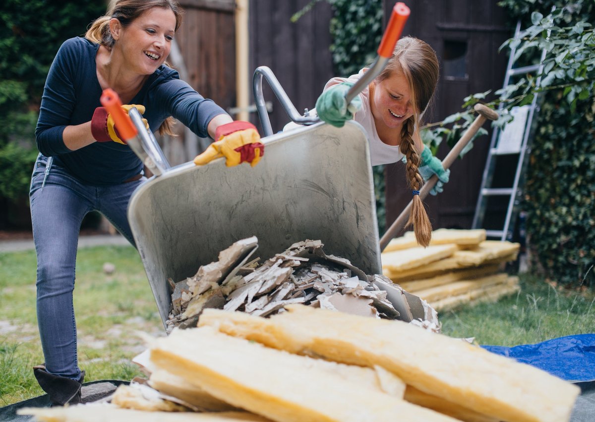 Two women dumping home renovation scraps in a pile outside