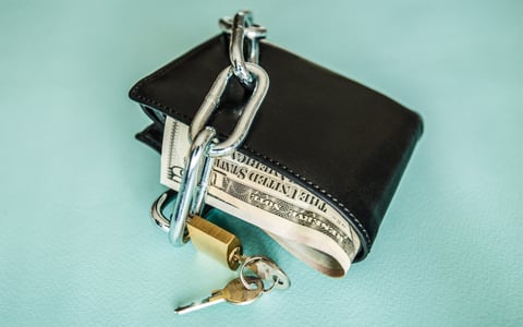 A wallet full of money is locked up with a chain and a padlock.