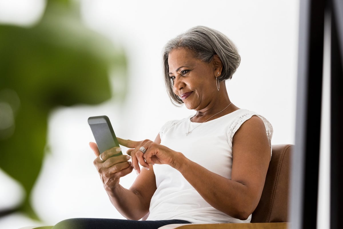 A woman sits and looks at her phone while smiling.