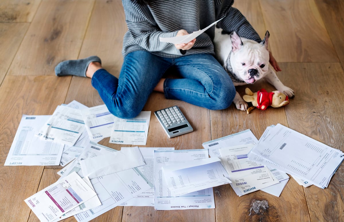 A woman and dog sitting on the floor surrounded by papers and a calculator.