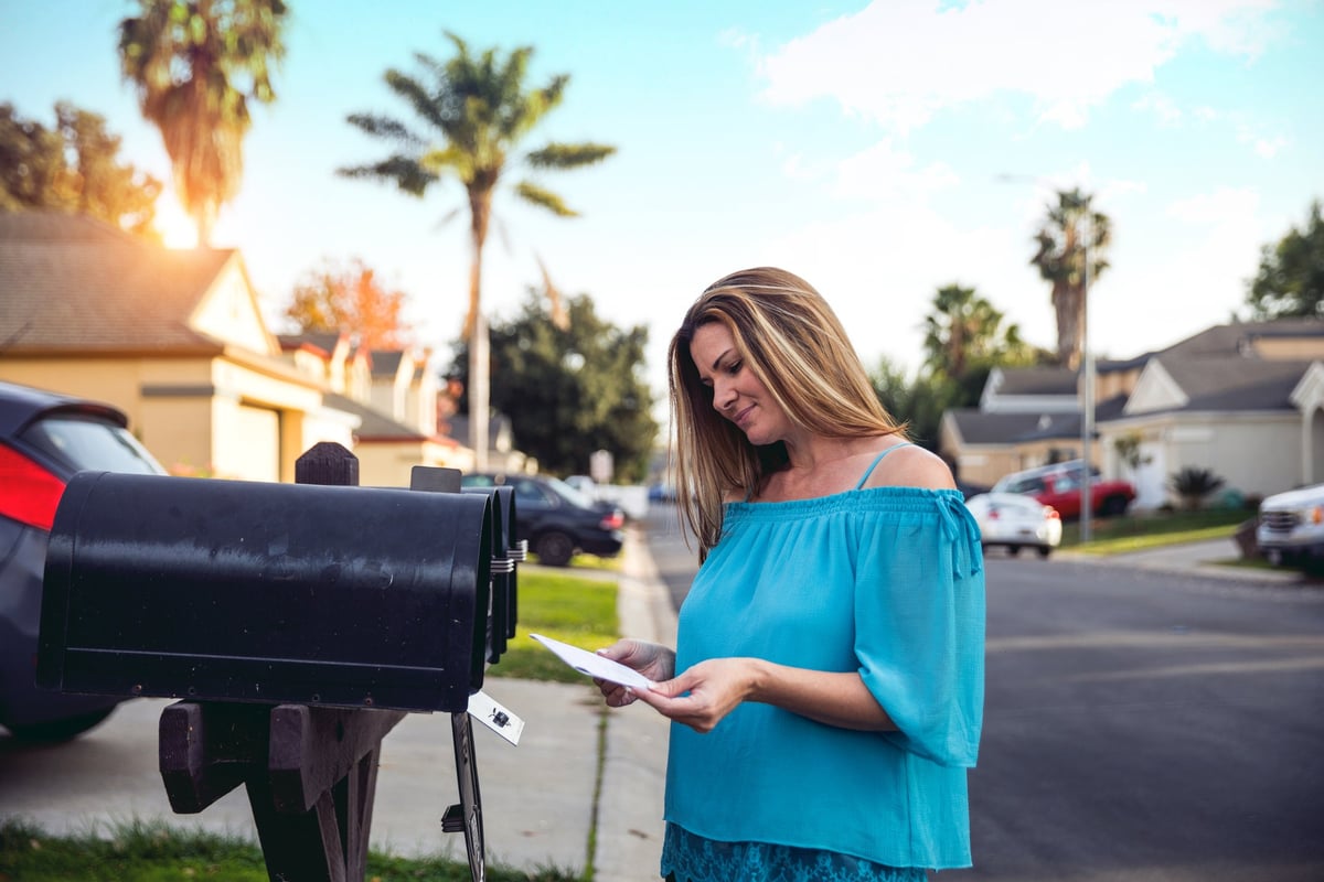 Woman checking mailbox in neighborhood with palm trees.