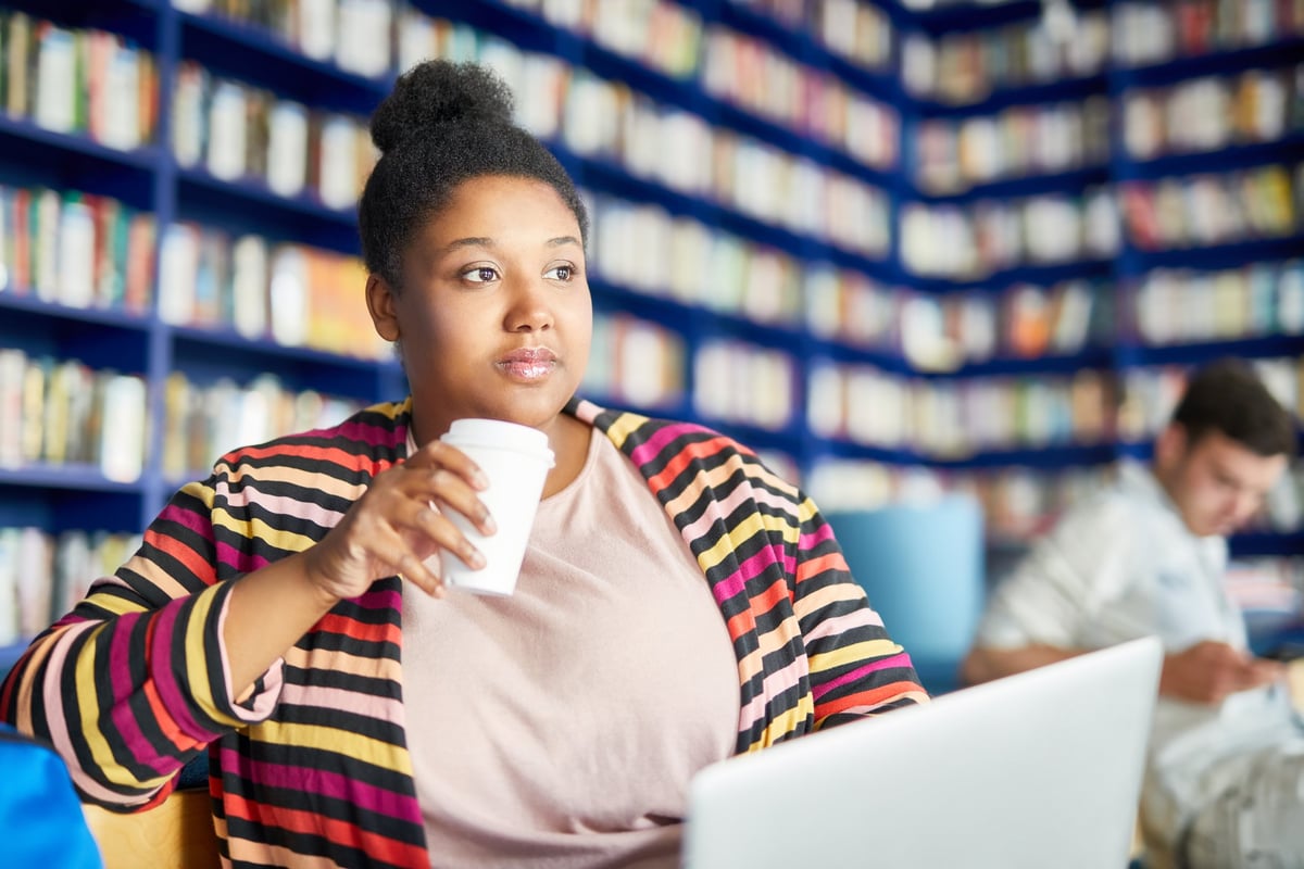 A student drinks coffee in the library.