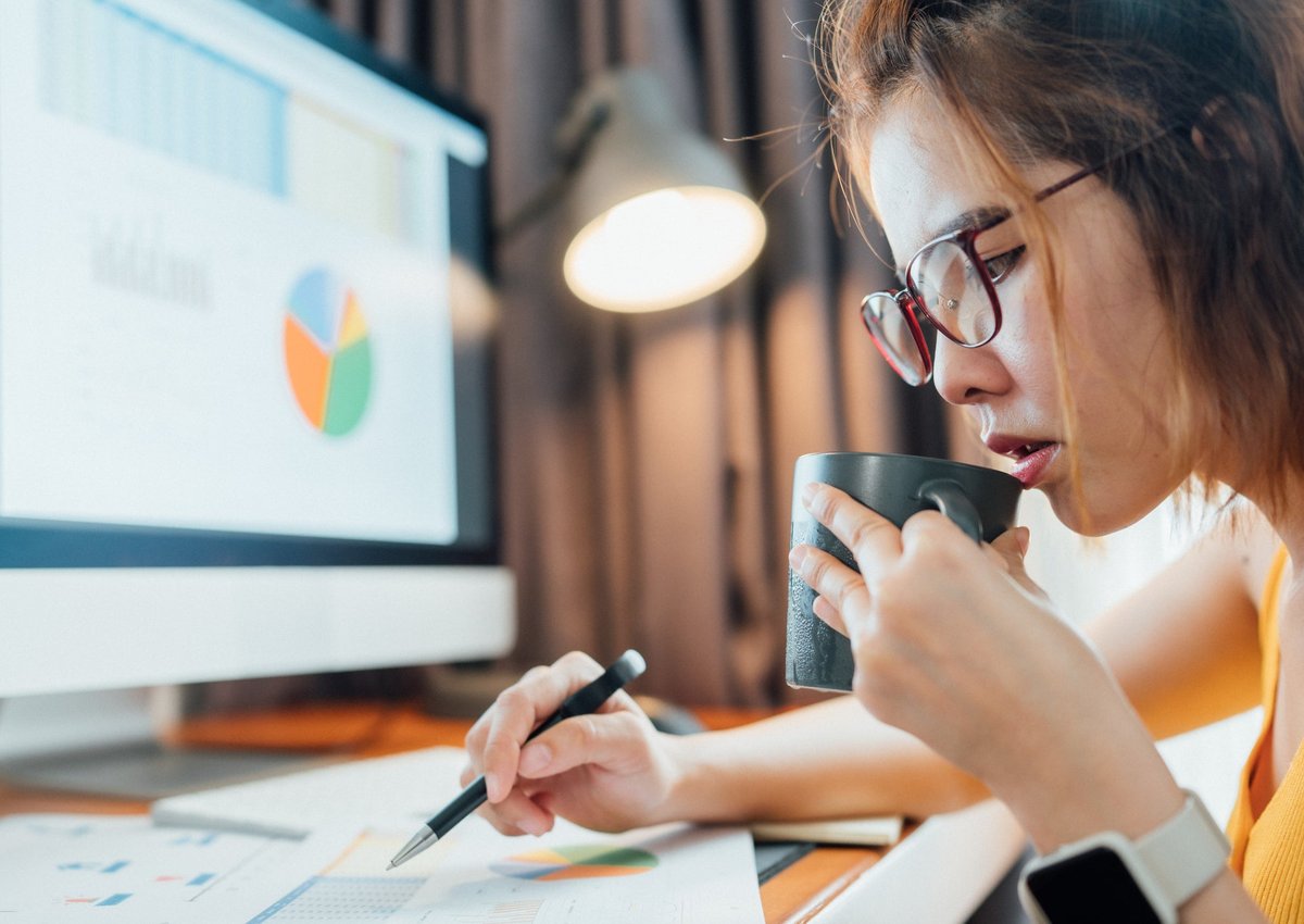 A woman sits at her computer, drinking coffee and going over her personal finances.