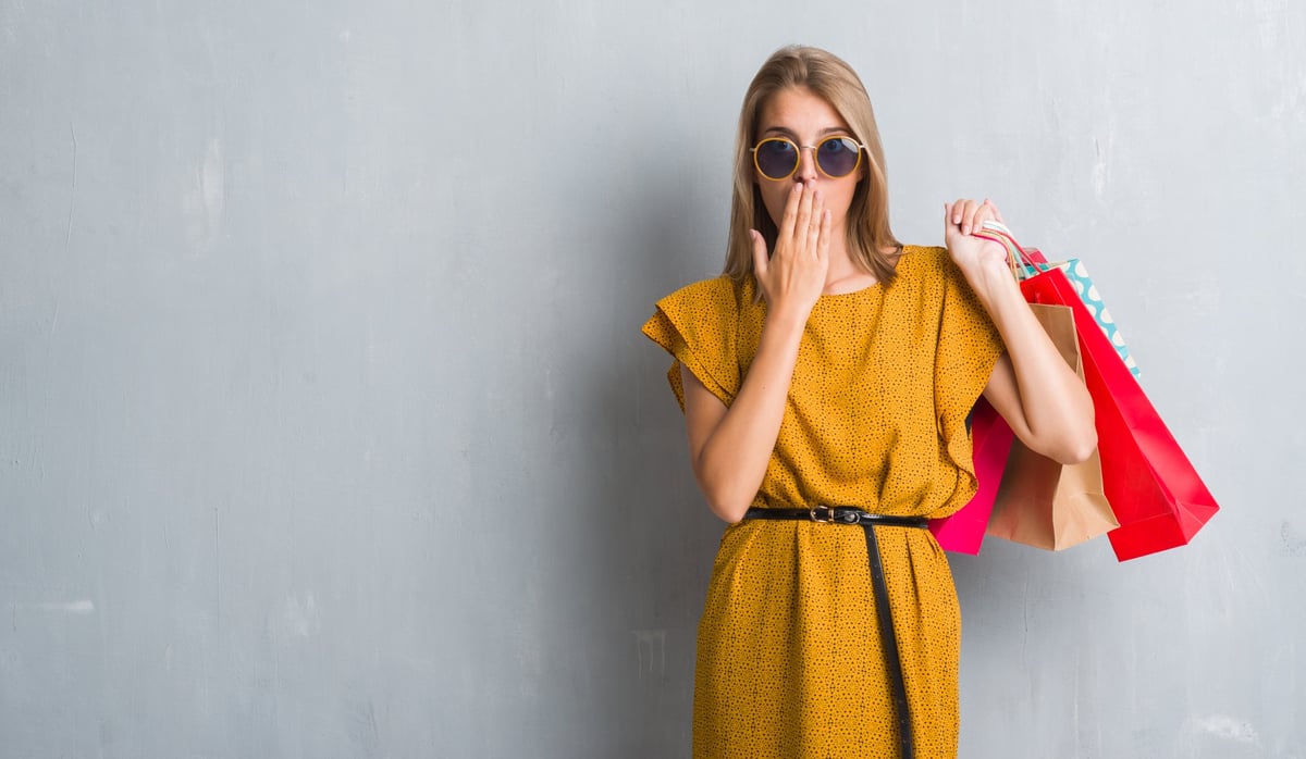 A woman holding shopping bags with her hand over mouth.