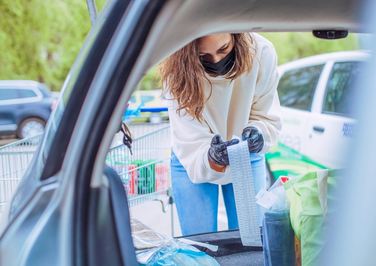 Woman loading car with groceries looks over her receipt closely.
