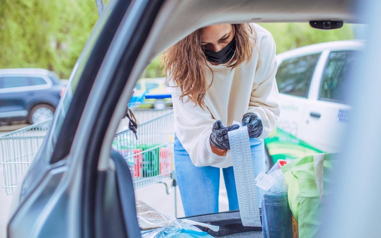 A woman loads groceries into the car and watches their delivery closely.