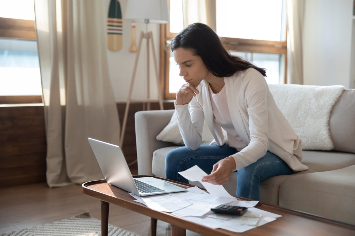 A young woman looks at her computer while trying to pay a pile of bills