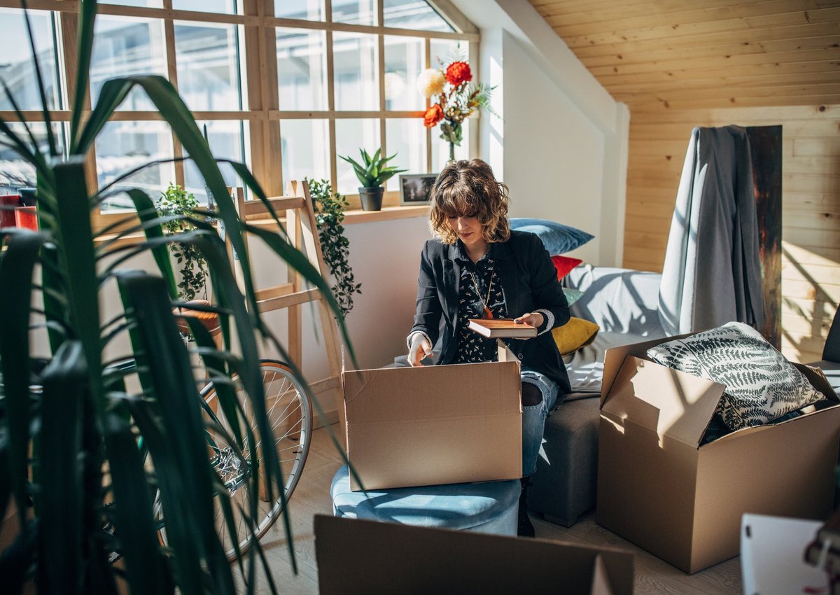 A young woman is moving into her new home. She is sitting in a room filled with plants, unpacking.