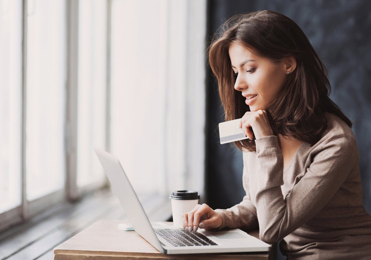 A woman using a laptop and holding a credit card.
