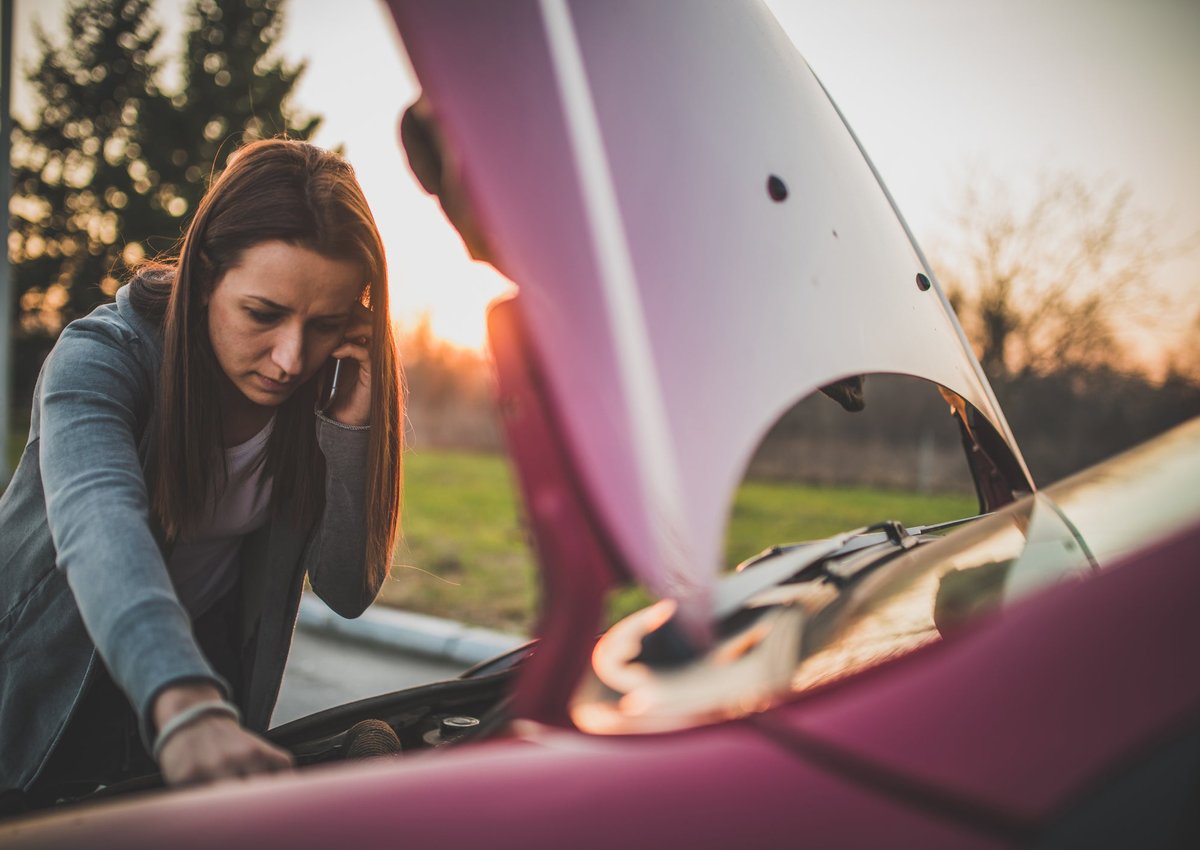 Woman on phone looking under hood of her car