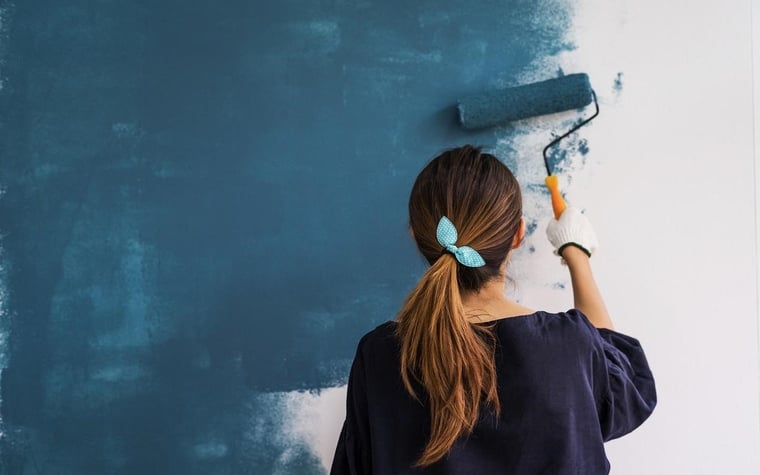 Woman painting home blue with a roller.