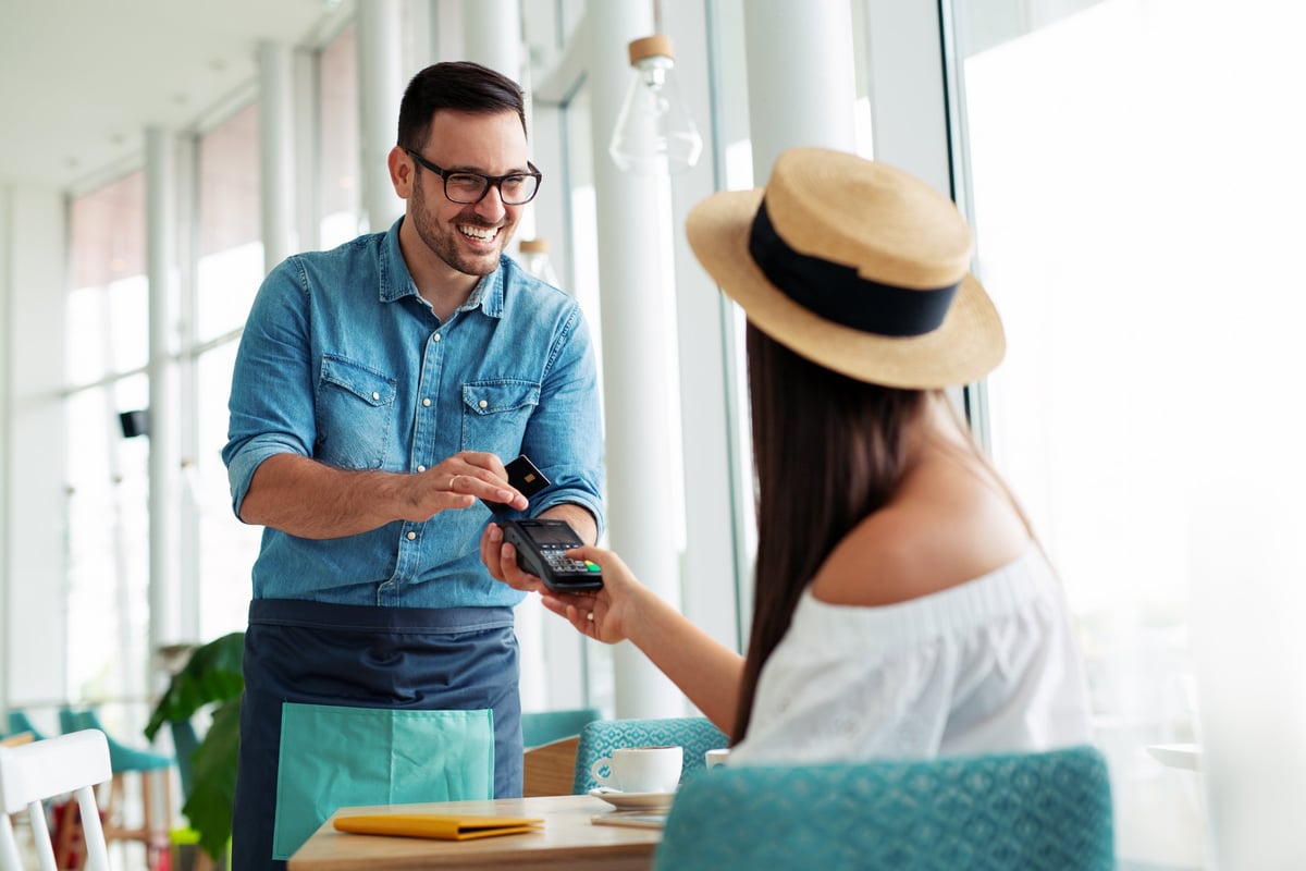 A young woman in a hat paying a waiter with her credit card.