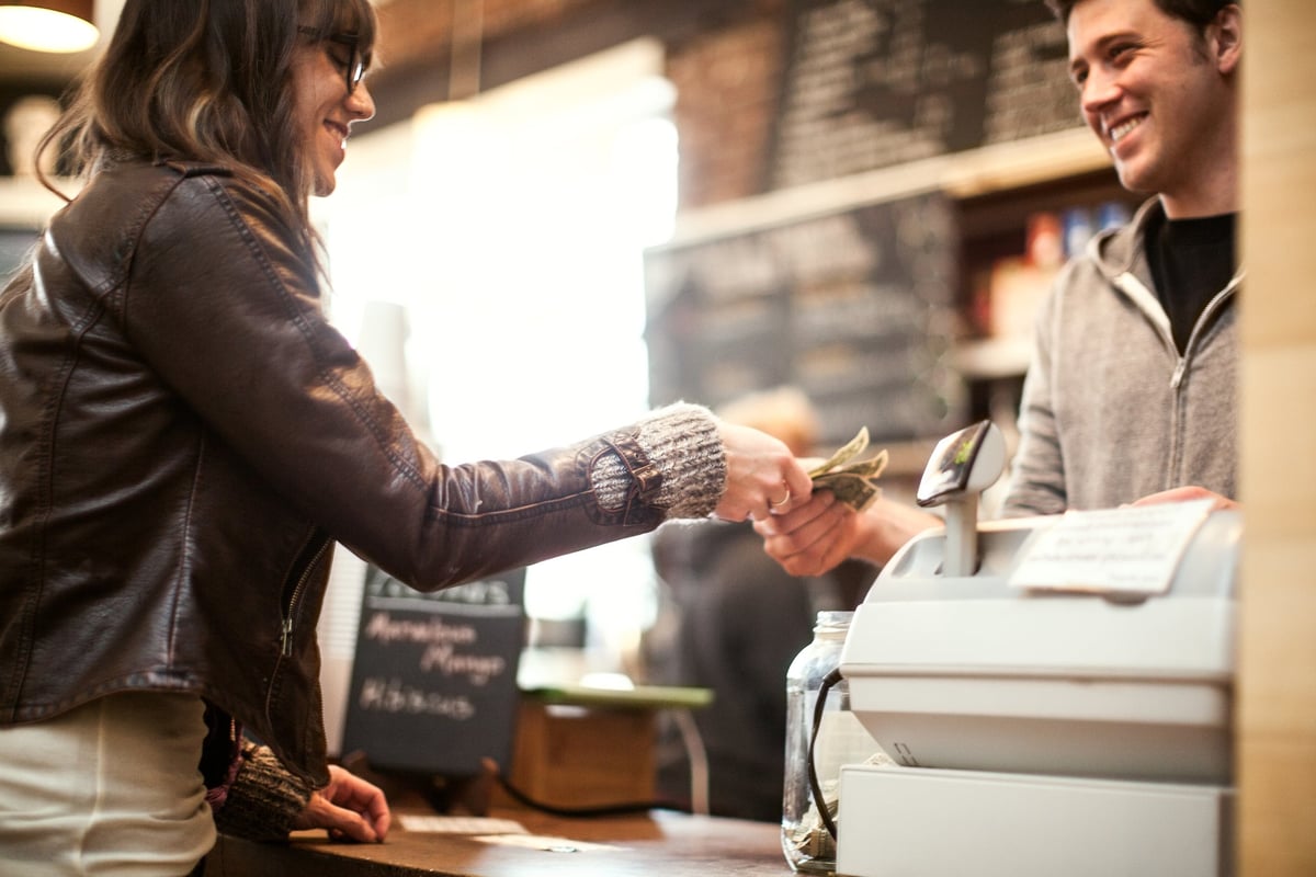 A smiling woman hands cash over to a cashier