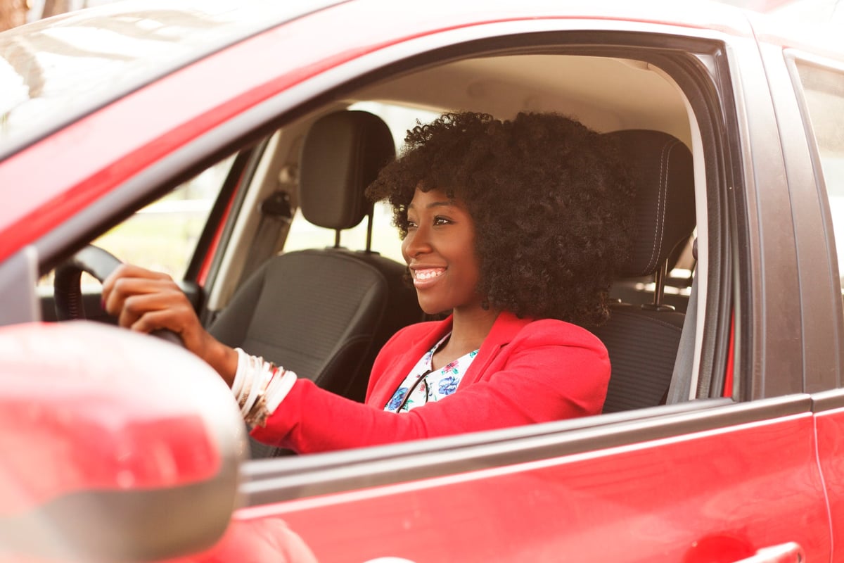 Woman smiling while driving a red vehicle.