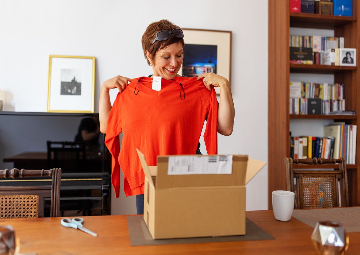 Woman smiling as she holds up sweater she purchased for herself.