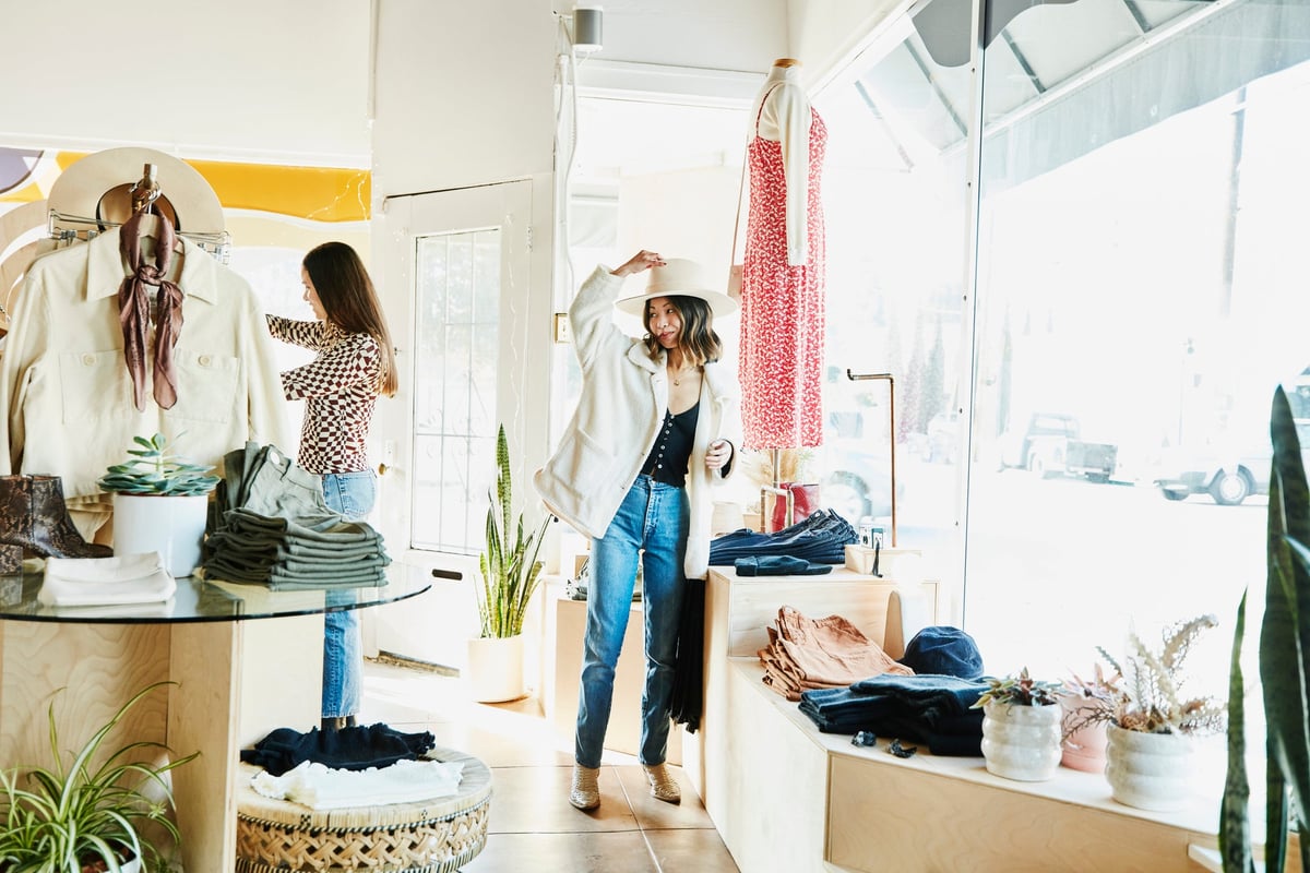 Woman trying on a hat while shopping in a boutique with friends.