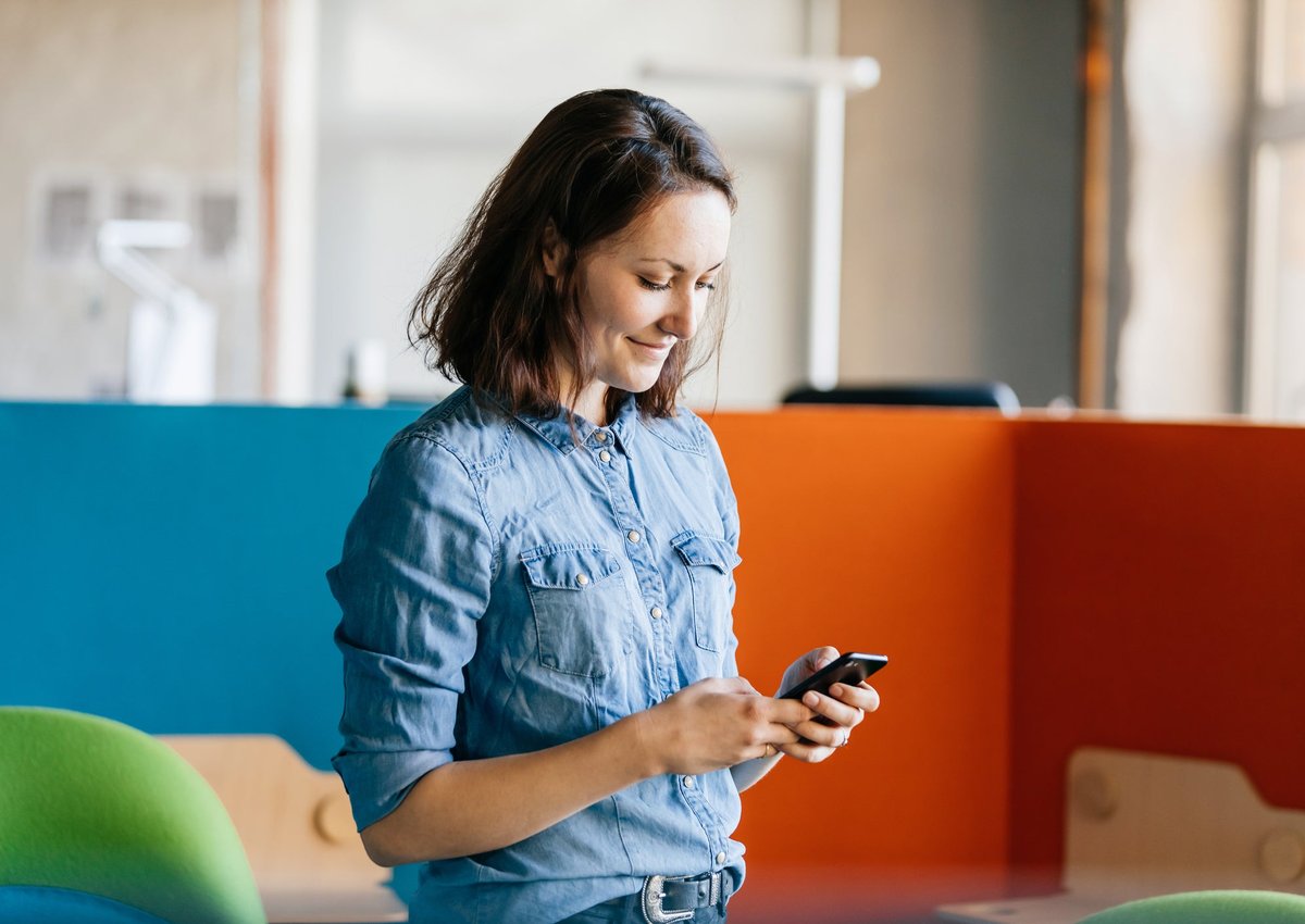 A woman stands at work, looking at her cellphone.