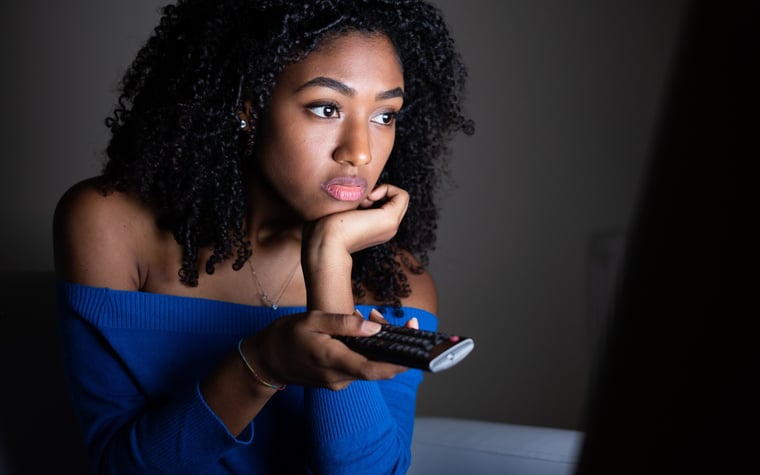 A young woman watching tv in a dark room.