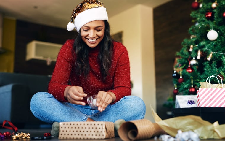 Femme portant un bonnet de Noel emballant des cadeaux.