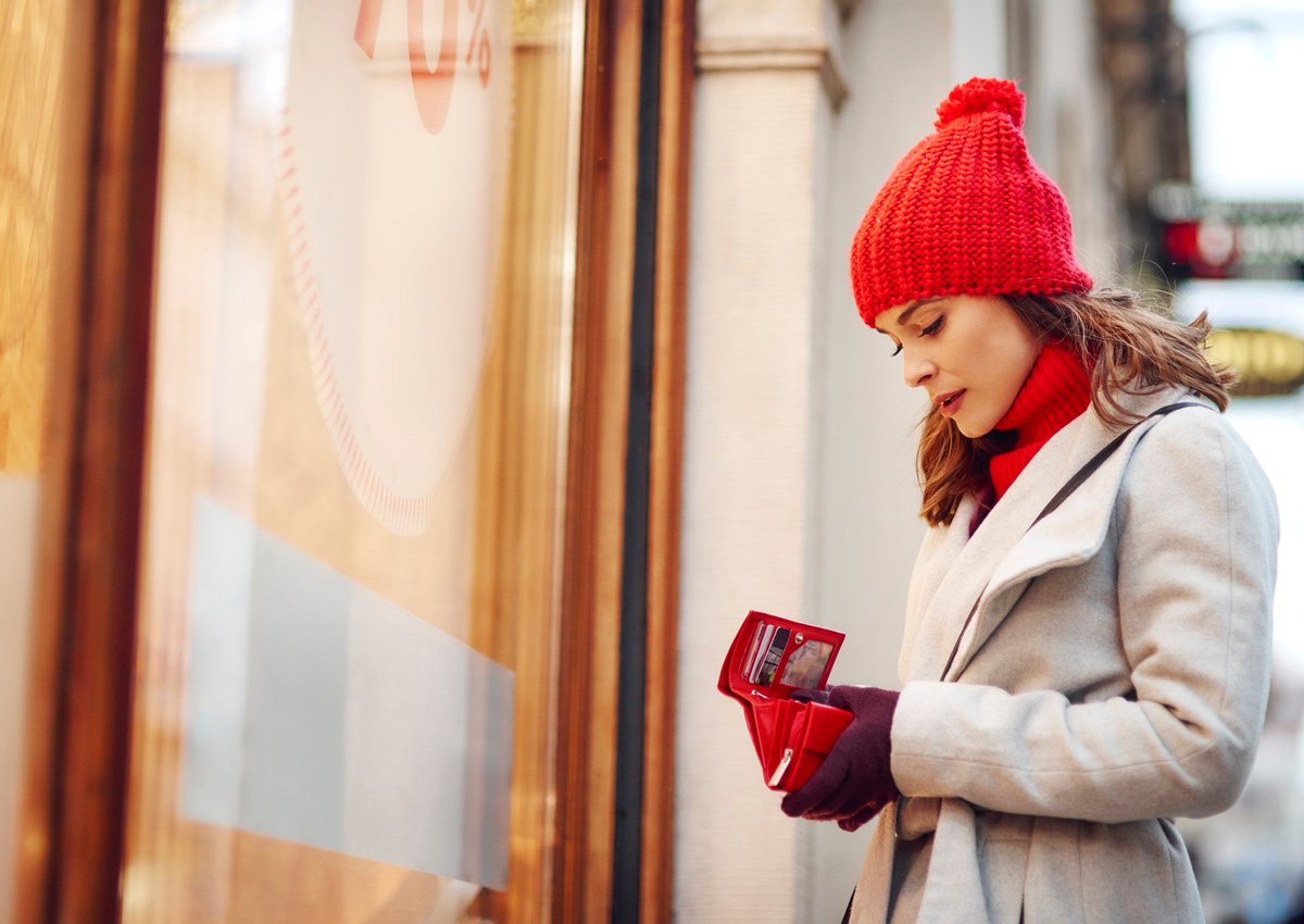 woman outside of a store looking into her empty wallet.