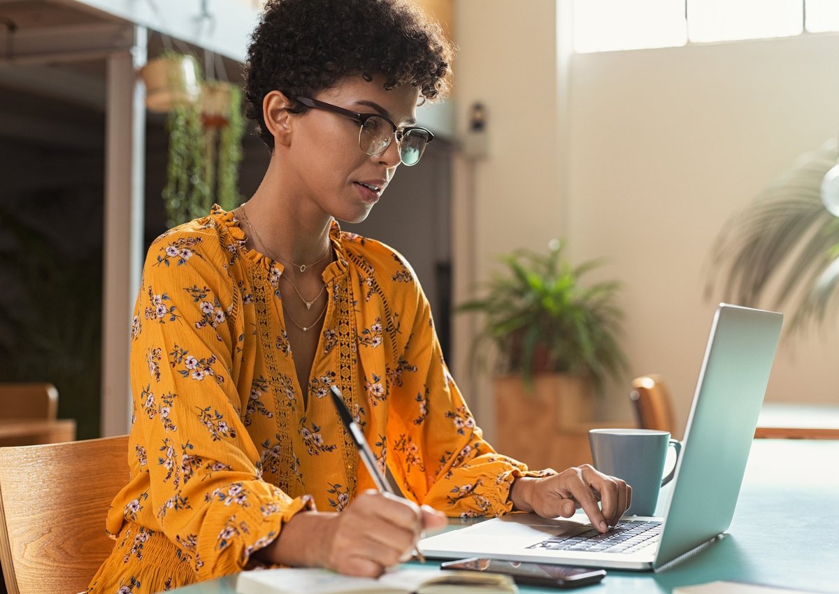 A female college student taking notes while studying on a laptop.
