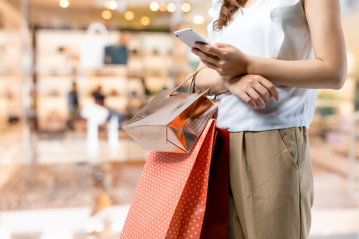 A woman is holding shopping bags and looking at her phone.