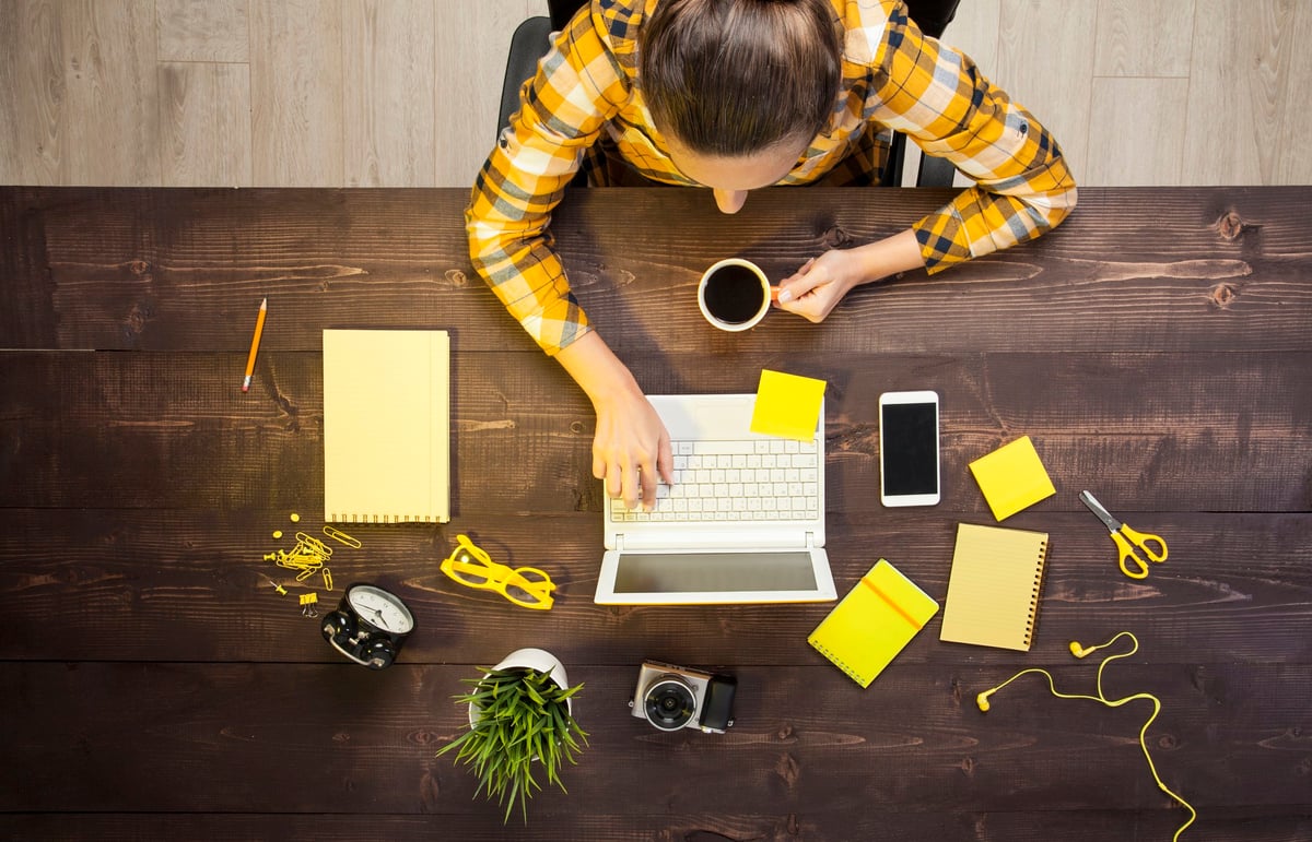 A woman working on a laptop with notepads and other desk items around her.