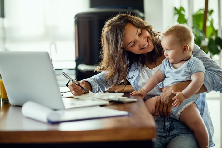 Woman working on taxes while holding infant in her lap.