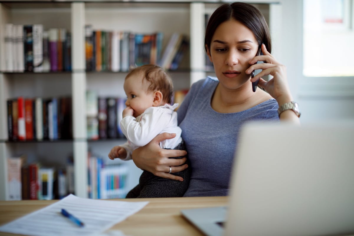 A woman works out of her home office while also caring for a child.