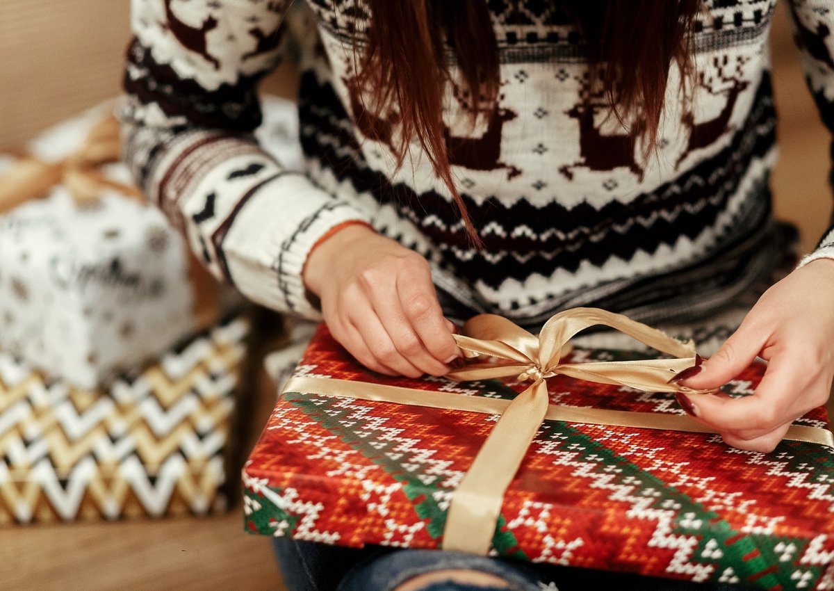A woman in a festive sweater wrapping gifts.