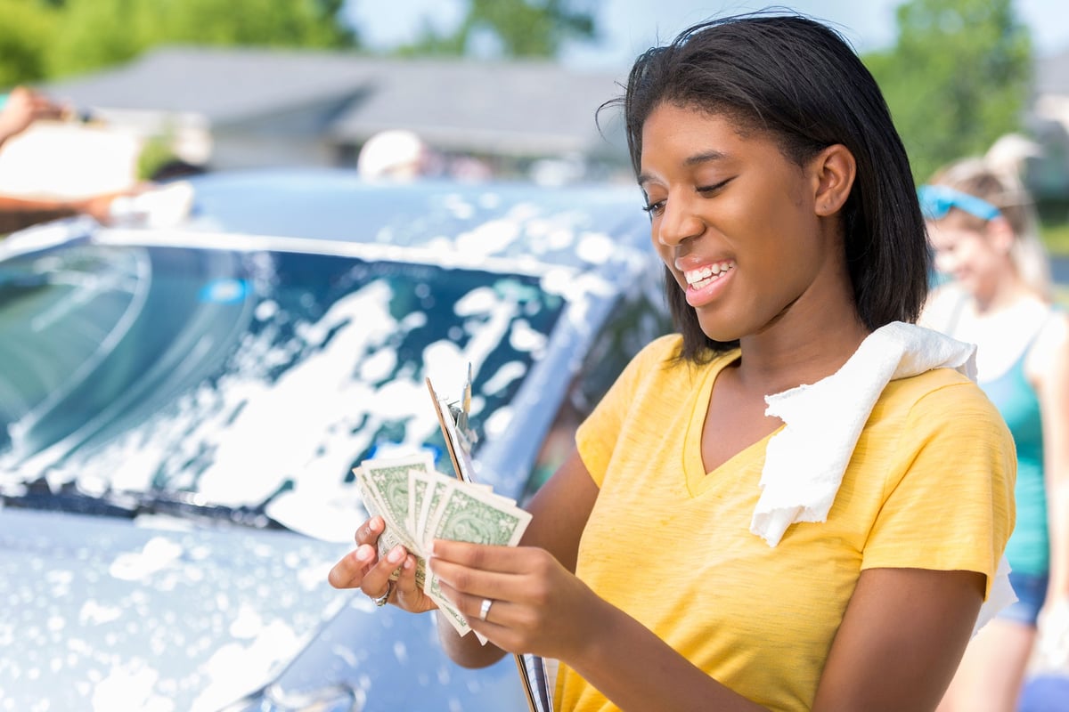 Young adult woman counts cash at car wash