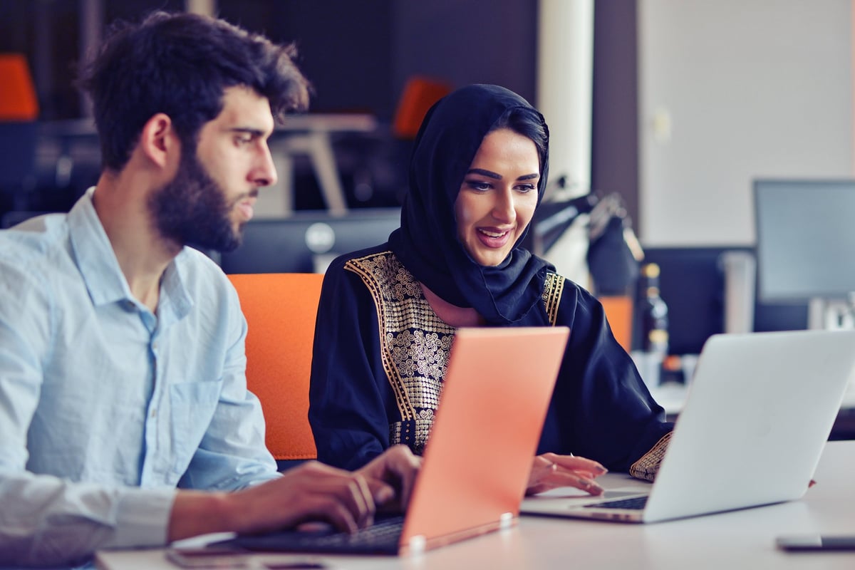 A young man and woman are working on a laptop next to each other.