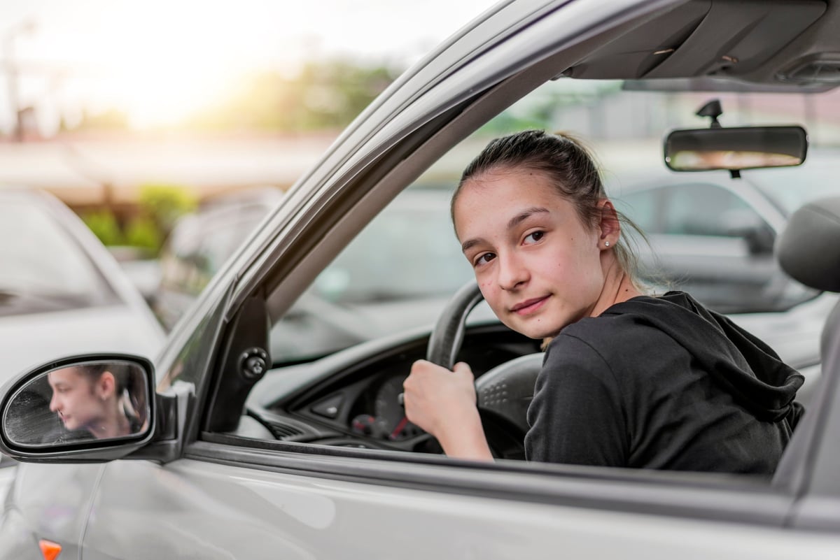 A young driver looks behind her before backing out of a parking spot.