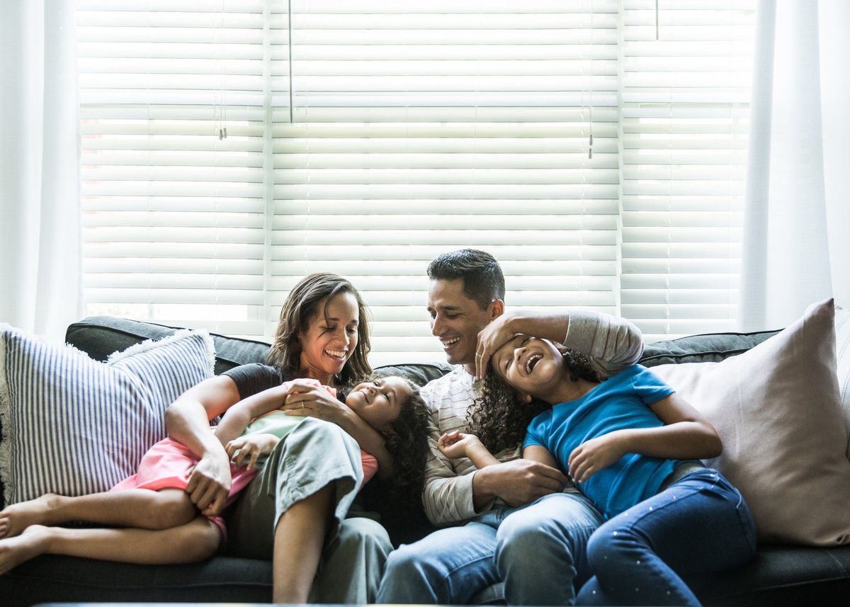 A young couple sit happily on a sofa with their two daughters.