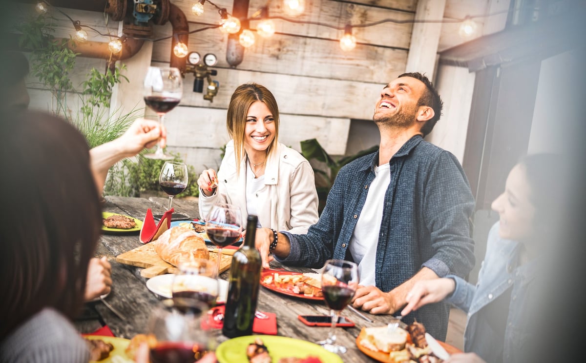 A group of smiling people having wine and food at a patio table.