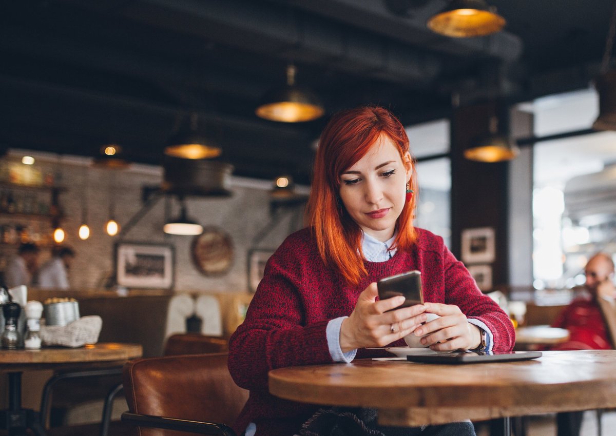 A young woman at a coffee shop looking at her phone.