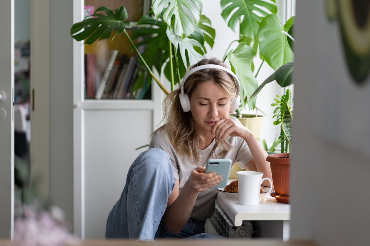 Young woman listening to podcast on her headphones while drinking coffee.