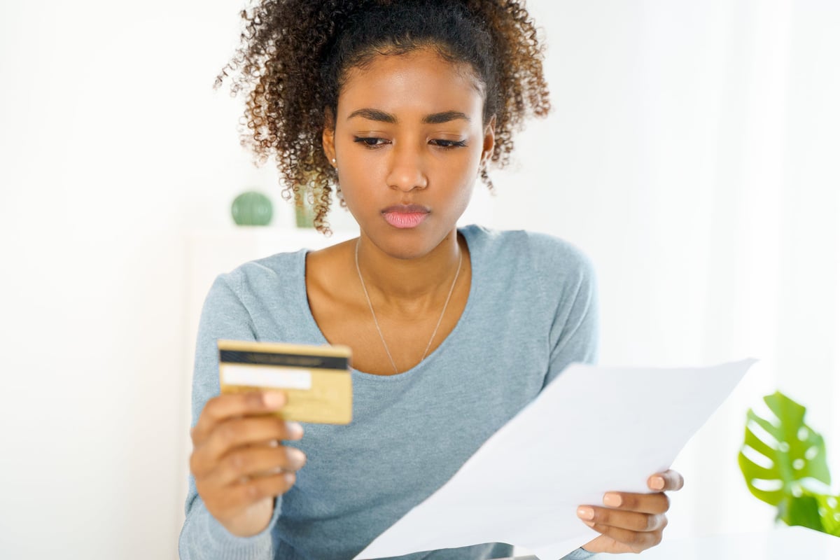 A young woman with a serious look on her face stares at her credit card.