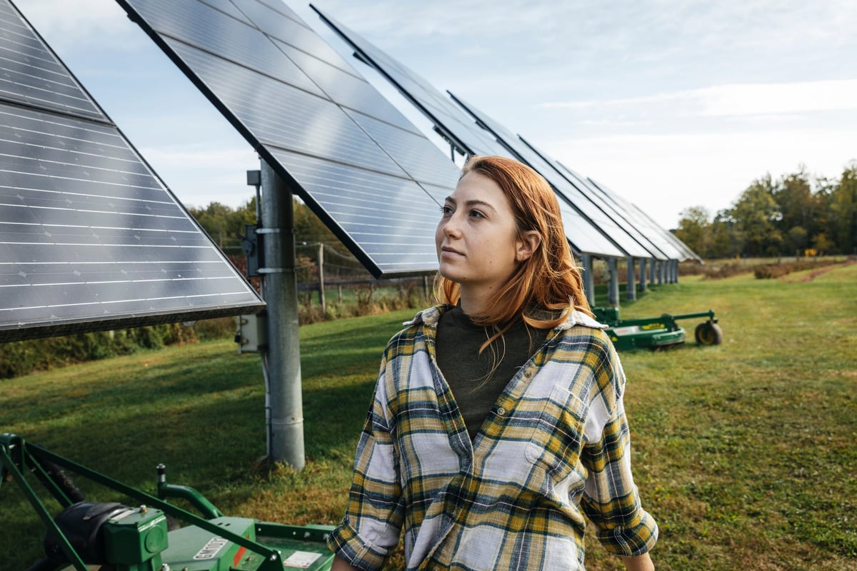 A young woman walks outside, looking at solar panels.