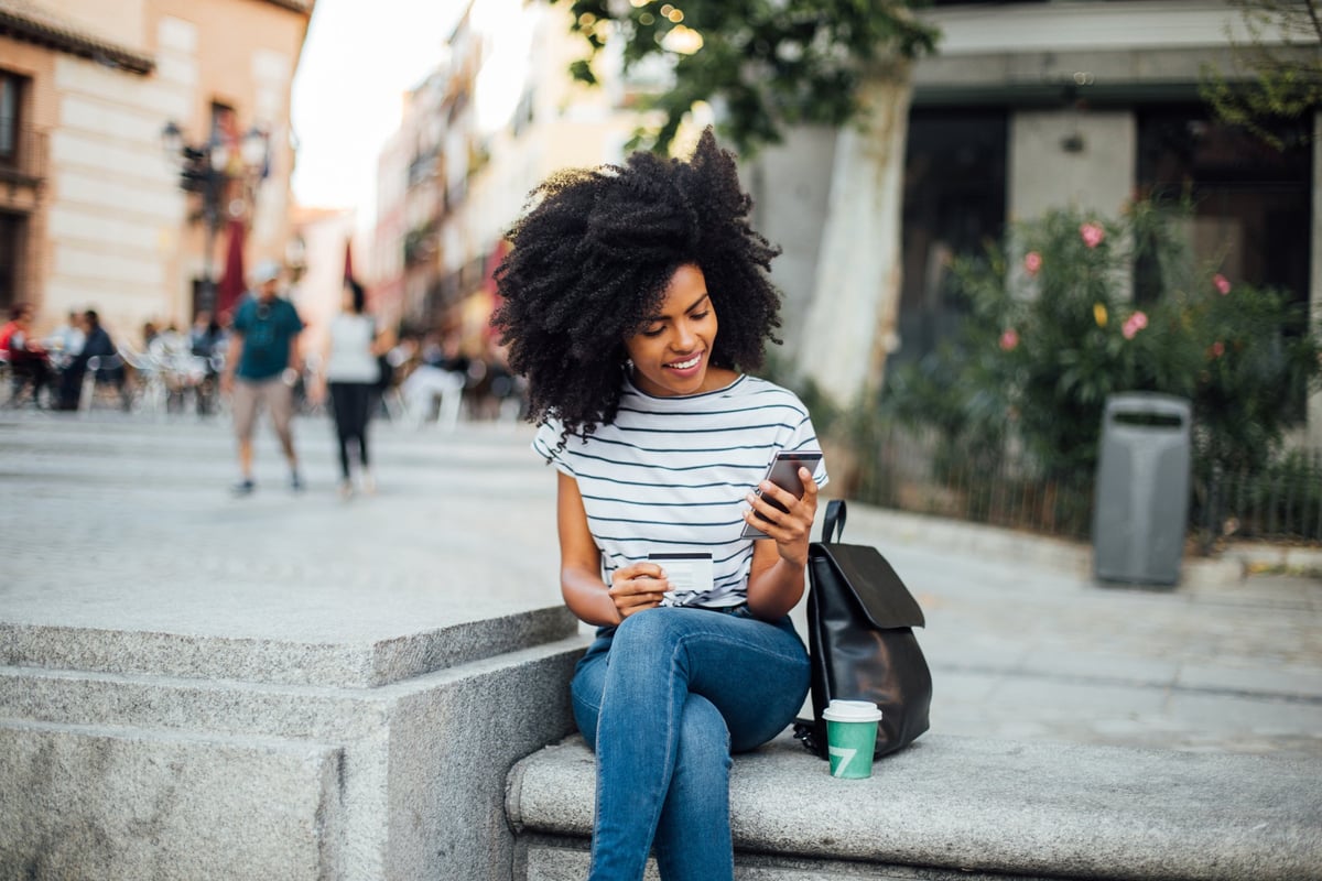 A young woman makes an online purchase while sitting outside.
